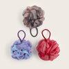 Three exfoliating mesh bath sponges in shades of gray, blue, and pink, tied with black string.