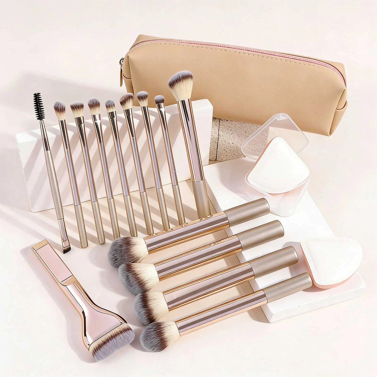 A collection of 17 makeup brushes and a powder puff in various shades of gold and natural hair color displayed on a white sur