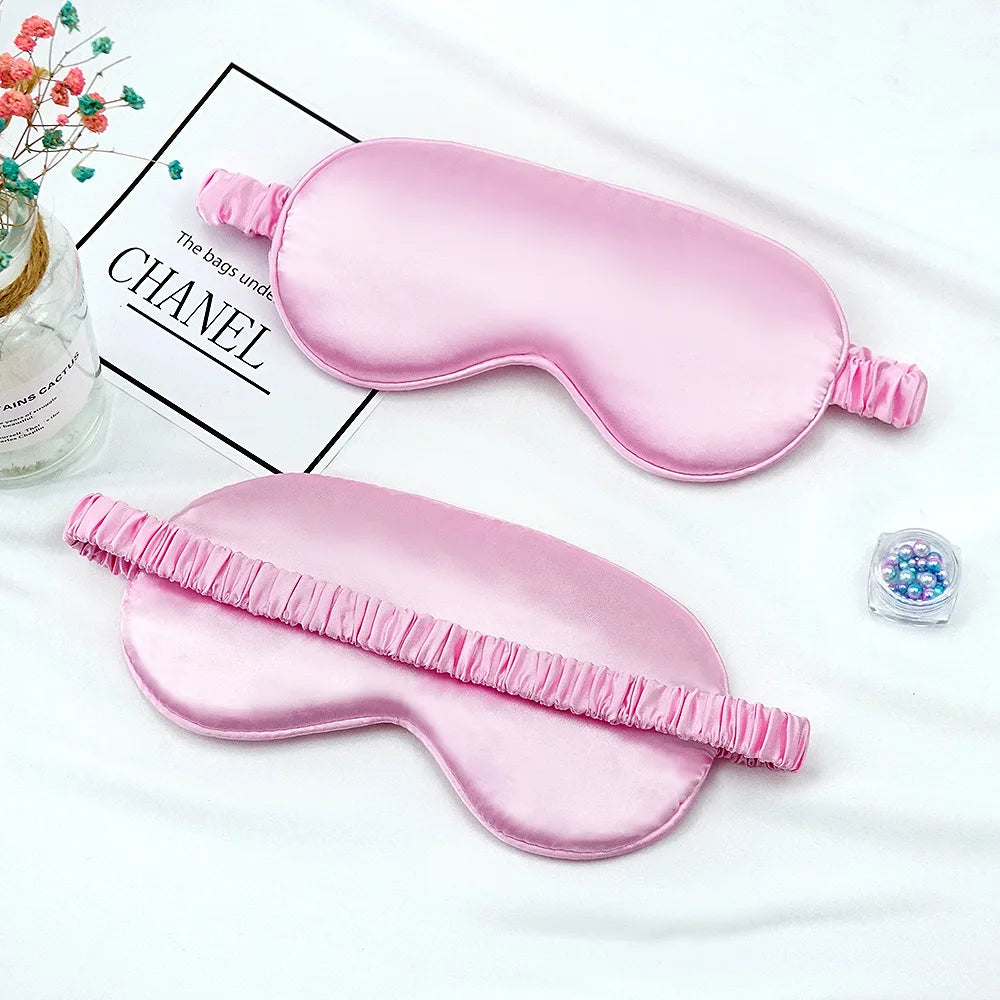 Masque de sommeil imitation soie rose avec bords froncés, présenté sur fond blanc.
