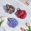 Three exfoliating mesh bath sponges in shades of gray, red, and purple resting on a white marble surface.