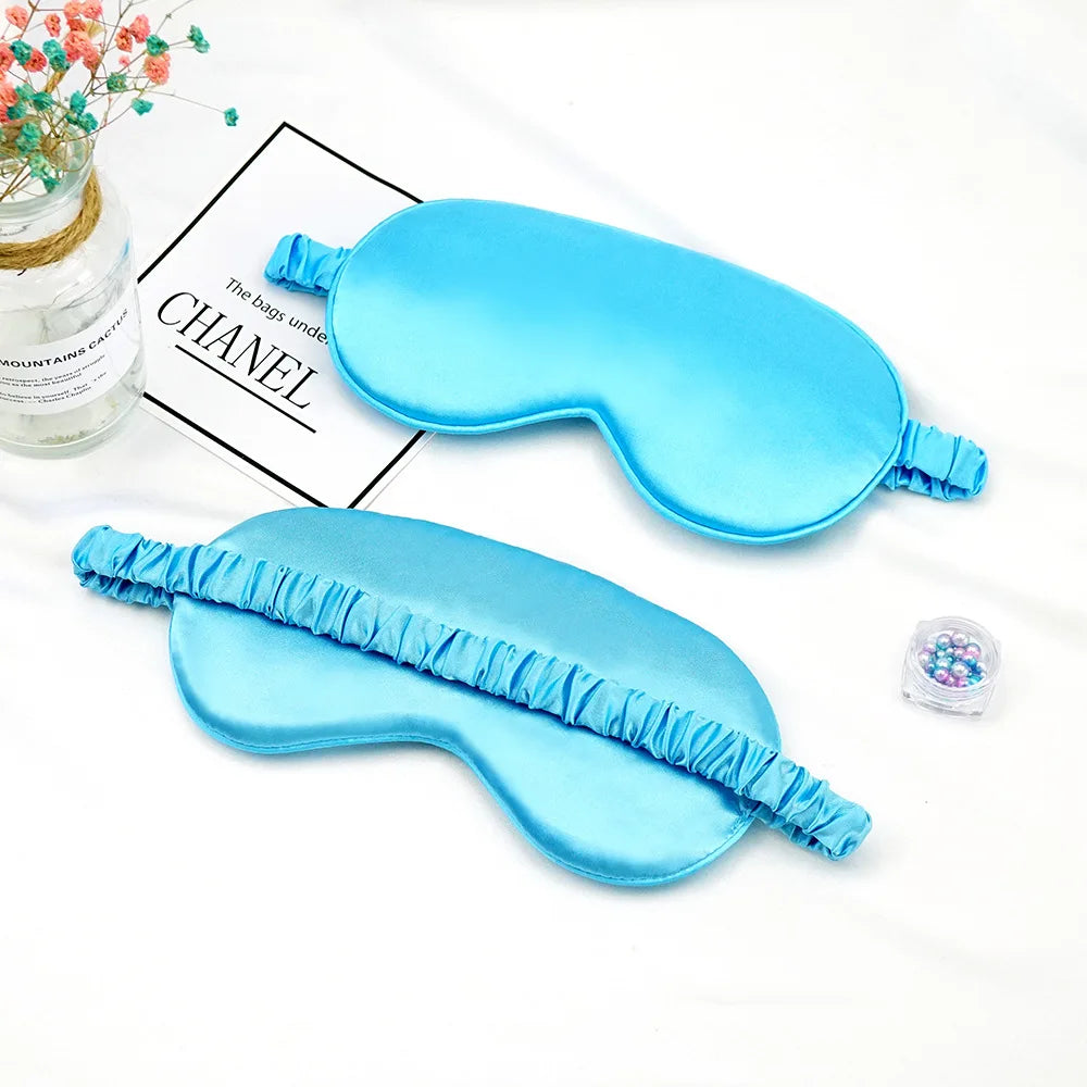 Deux masques pour les yeux en soie bleu clair sont présentés sur un fond blanc avec un pot en verre et un petit sachet.