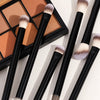 A set of black makeup brushes with soft, fluffy bristles displayed next to an open palette.