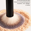 A close-up of a black makeup brush with soft bristles is shown above a mound of light pink cosmetic powder.