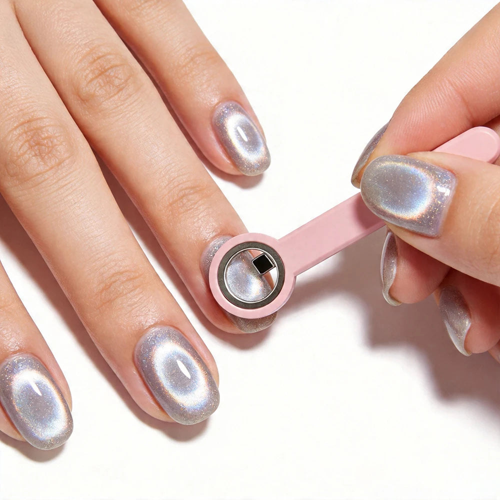 A hand holds a pink magnetic nail art stick with iridescent silver polish on manicured nails.