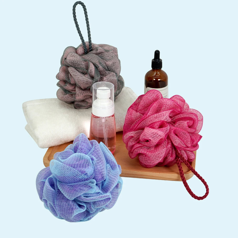 A collection of exfoliating mesh bath sponges in purple, pink, and blue colors with a glass dropper bottle nearby.