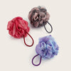 Three handmade exfoliating mesh bath sponges in shades of pink, gray, and purple