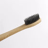 A wooden toothbrush with black bristles is shown on a white background.
