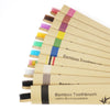 A row of ten bamboo toothbrushes with various colored bristles displayed on a light brown background.