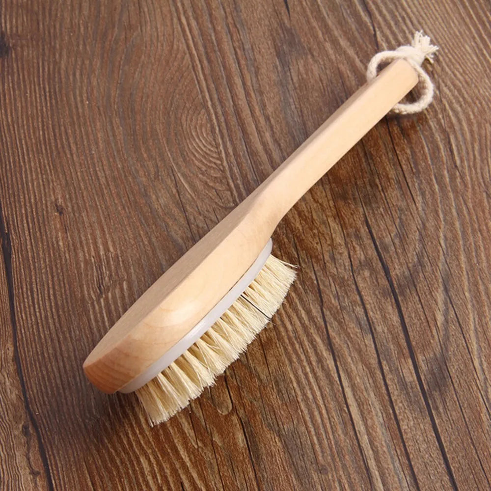 A light wooden body brush with natural bristles and a twine handle resting on a dark wooden surface.