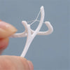 A hand holds a white disposable dental floss pick with a string of floss, demonstrating the product for oral hygiene.