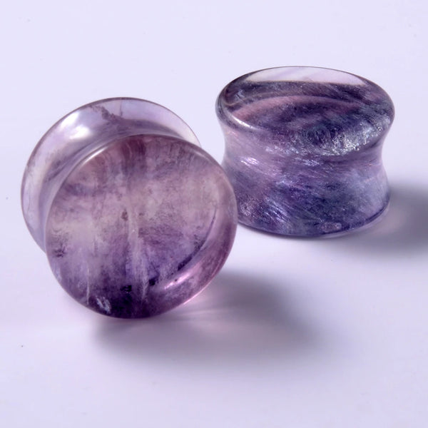 A close-up of a purple stone body piercing ear gauge with a smooth, polished surface.