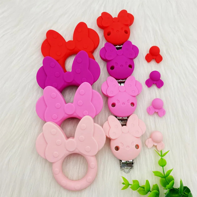 Une collection de perles de dentition en silicone dans diverses nuances de rose et de rouge sont présentées sur une surface b