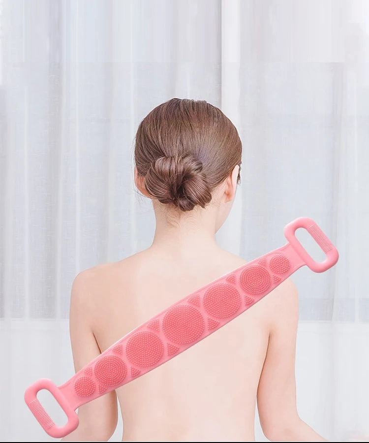 A pink silicone body scrubber and massage brush is shown on a person's back.