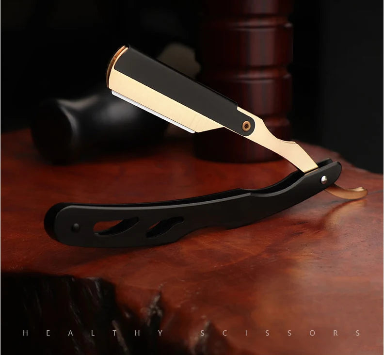 A professional straight edge barber razor with a black handle and gold accents resting on a wooden surface.