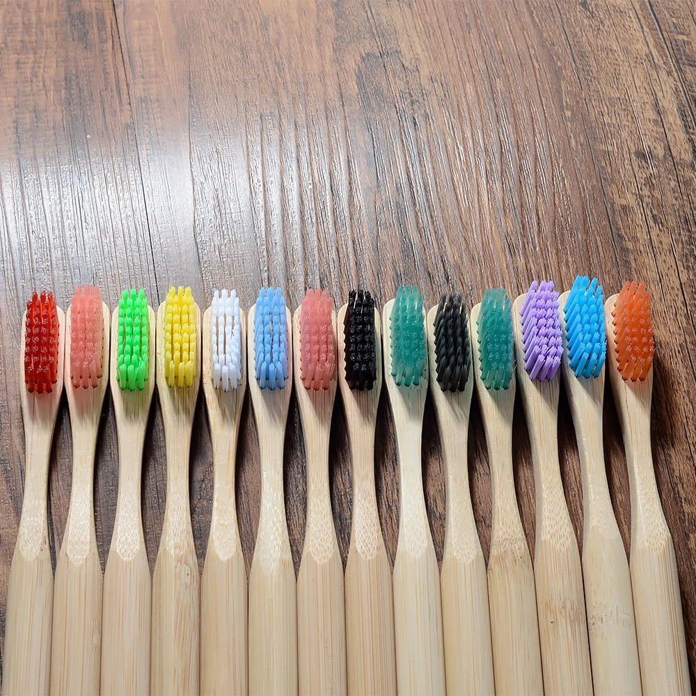 A row of ten eco-friendly bamboo toothbrushes in various colors is displayed on a wooden surface.