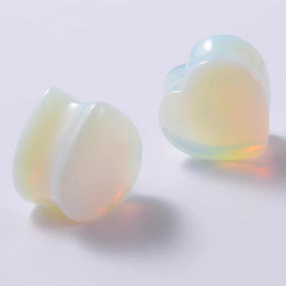 Un par de dilatadores de oreja en forma de corazón hechos de piedra translúcida azul verdosa pálida, proyectando una suave so