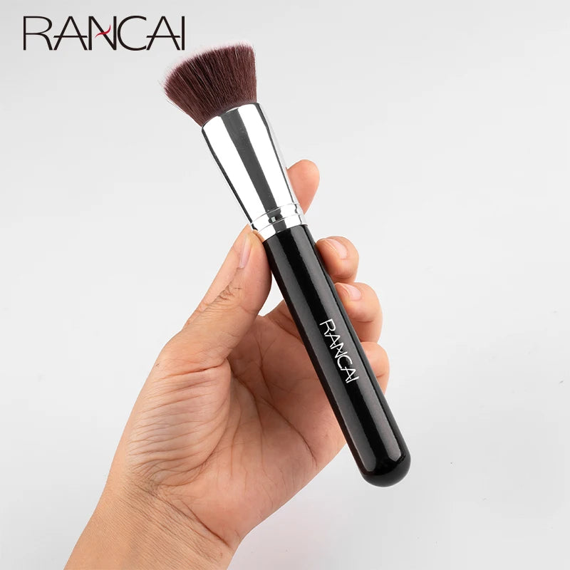 A black flat top kabuki foundation brush with a pink bristles is held in a hand.