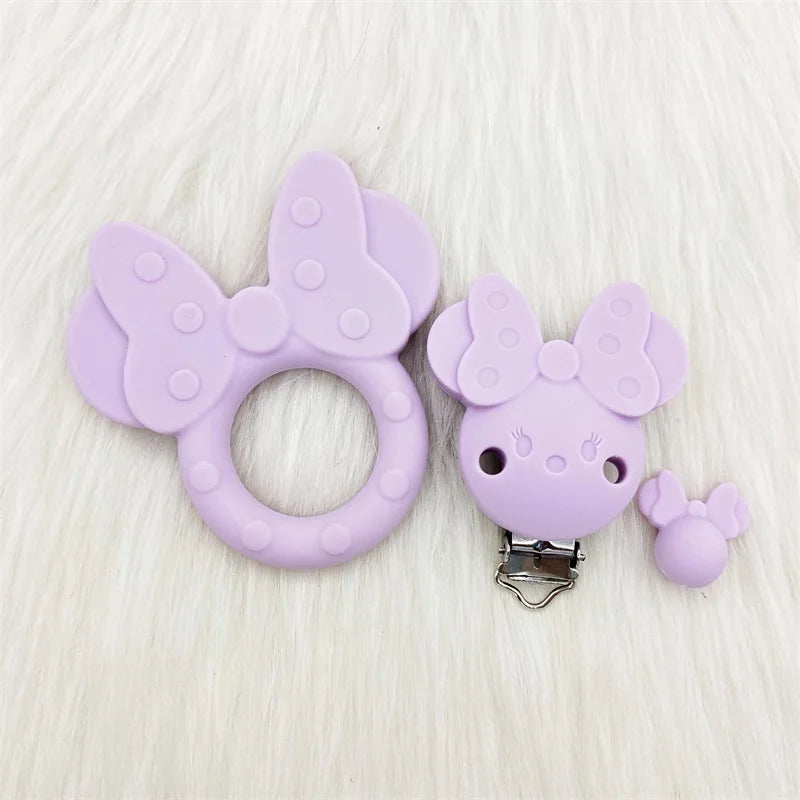 Un téthère en silicone violet en forme de papillon avec un petit charme pour les soins buccaux du bébé.