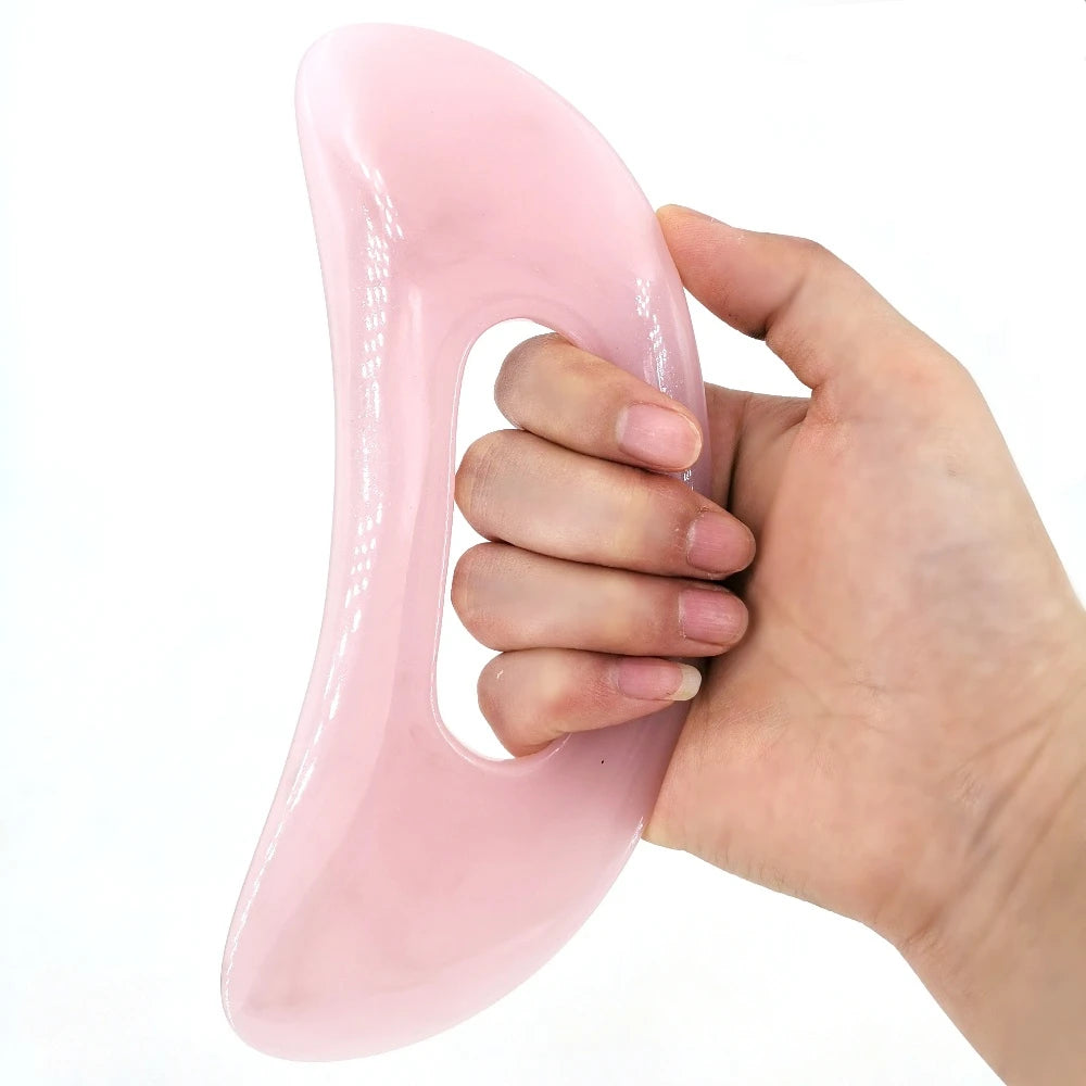 Une main tient un board de massage guasha en pierre naturelle rose et lisse.