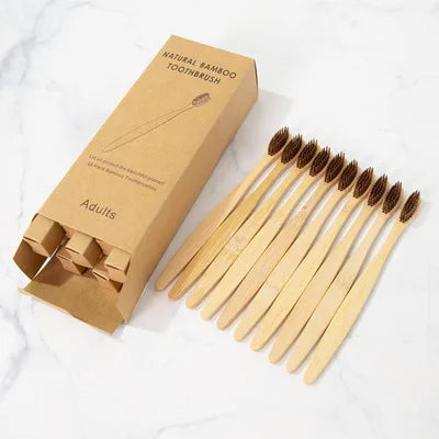 A box of natural bamboo toothbrushes for adults with individual wooden brushes displayed on a white marble surface.