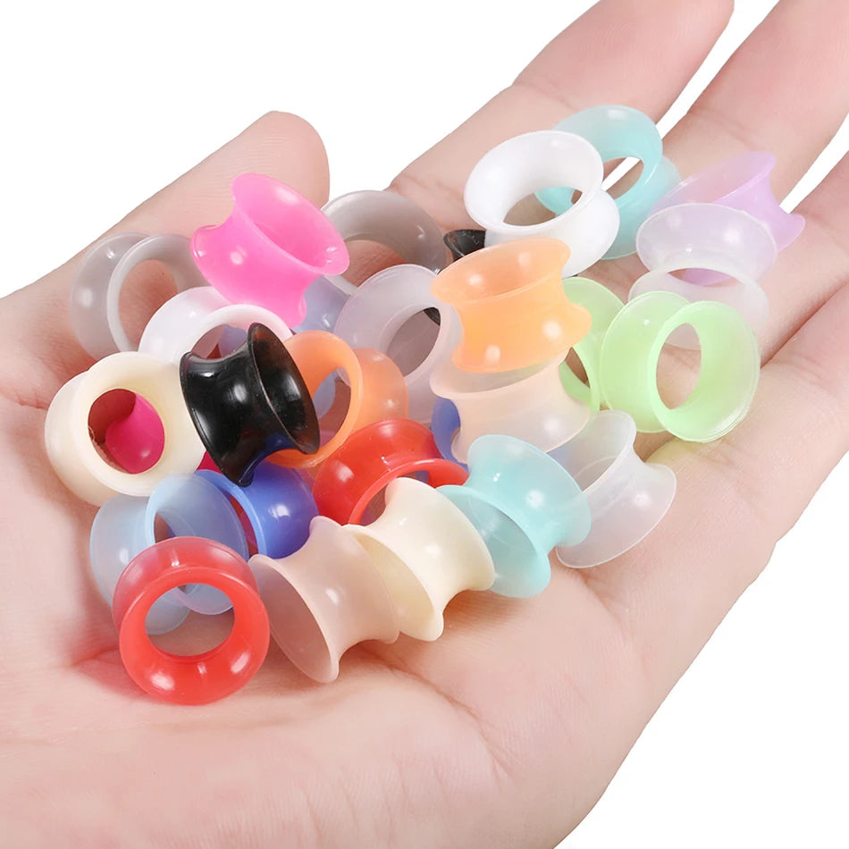 A hand holds a collection of colorful flexible silicone ear tunnels and plugs.
