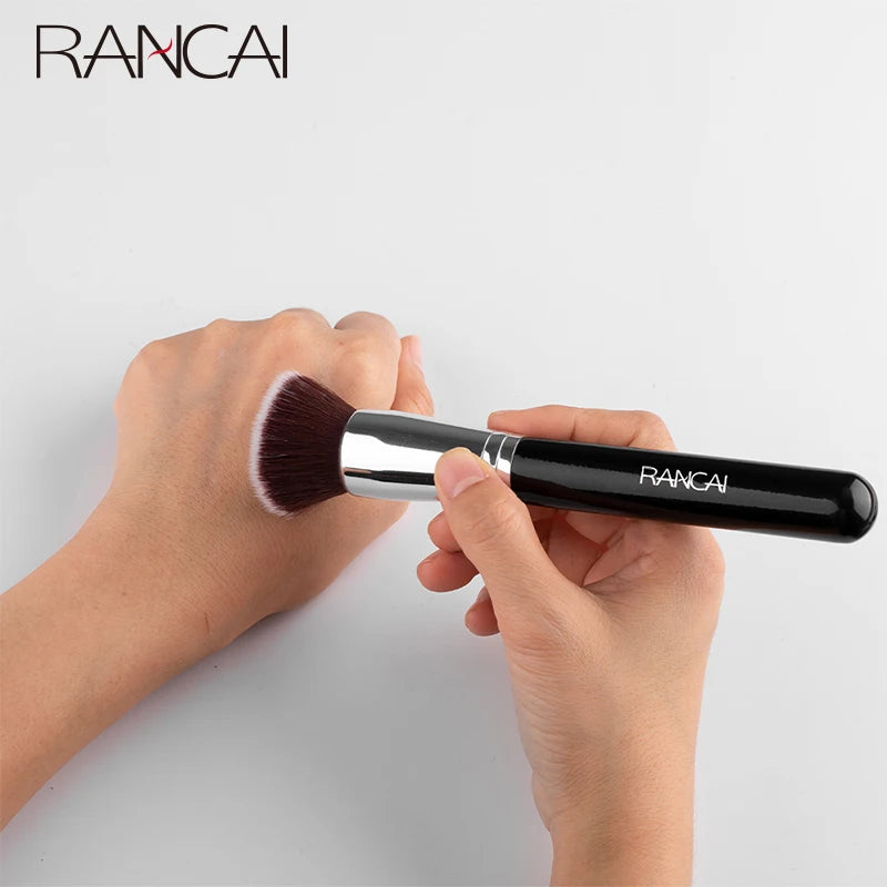 A hand is holding a black flat top kabuki foundation brush with a pink bristles against a white background.