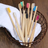 A collection of natural bamboo toothbrushes with various colored bristles displayed in a woven basket on a white cloth.