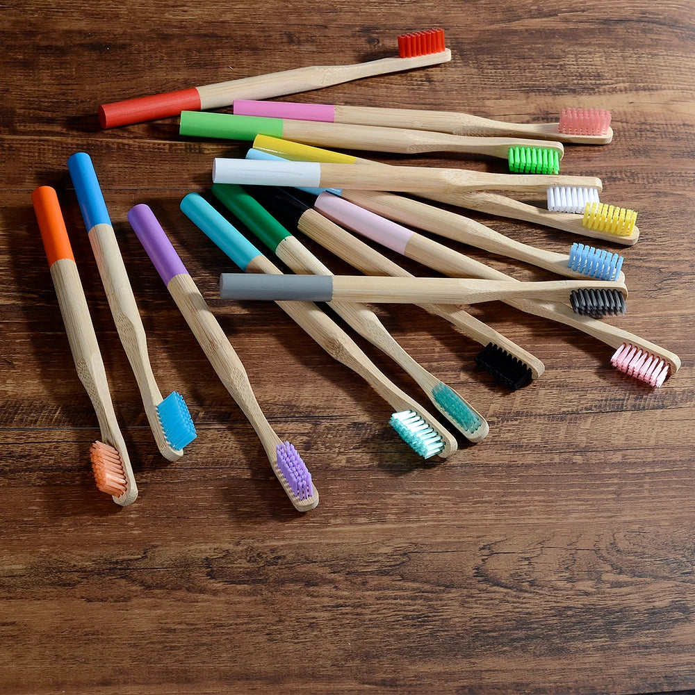 A collection of ten eco-friendly bamboo toothbrushes in various colors and bristles laid out on a wooden surface.