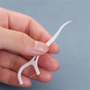 A hand holds a white dental floss pick with a curved tip against a light gray background.