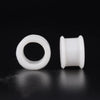A pair of white silicone ear tunnel plugs, one circular and one cylindrical.