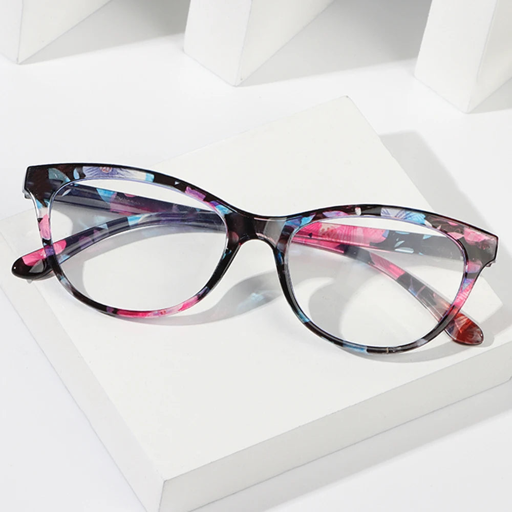 Un par de elegantes gafas de lectura florales anti-luz azul con detalles en morado y rosa sobre una superficie blanca.