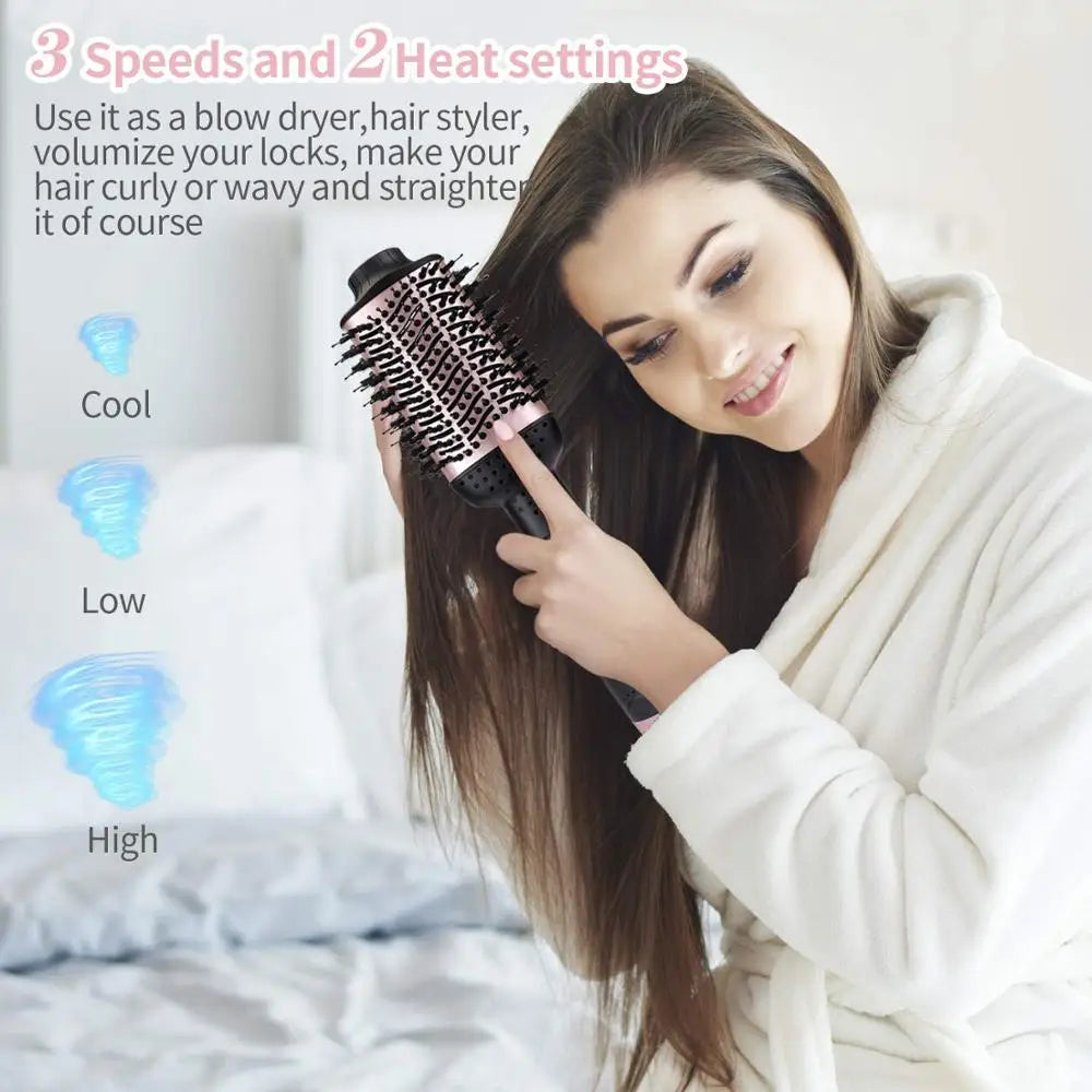 A woman uses a black styling brush on her long hair while sitting in bed.