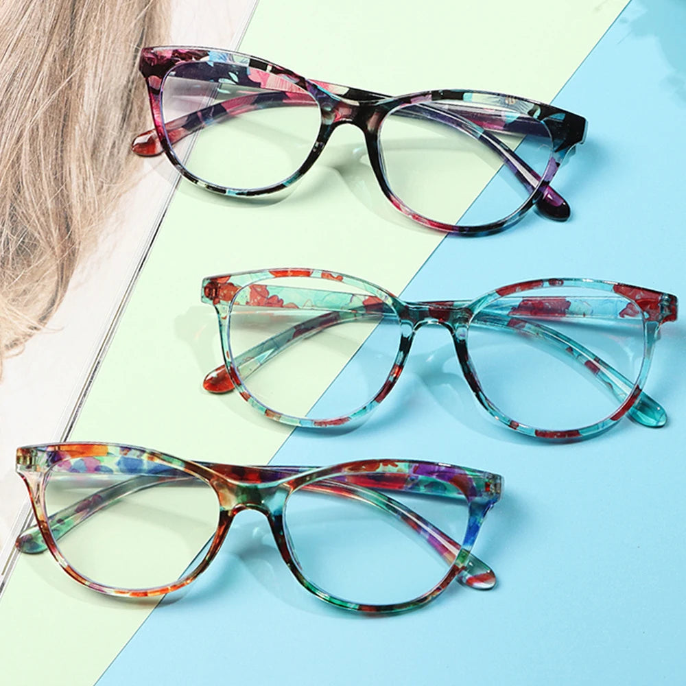 Un set de elegantes gafas de lectura anti-luz azul floral con lentes de varios colores sobre una superficie azul claro.
