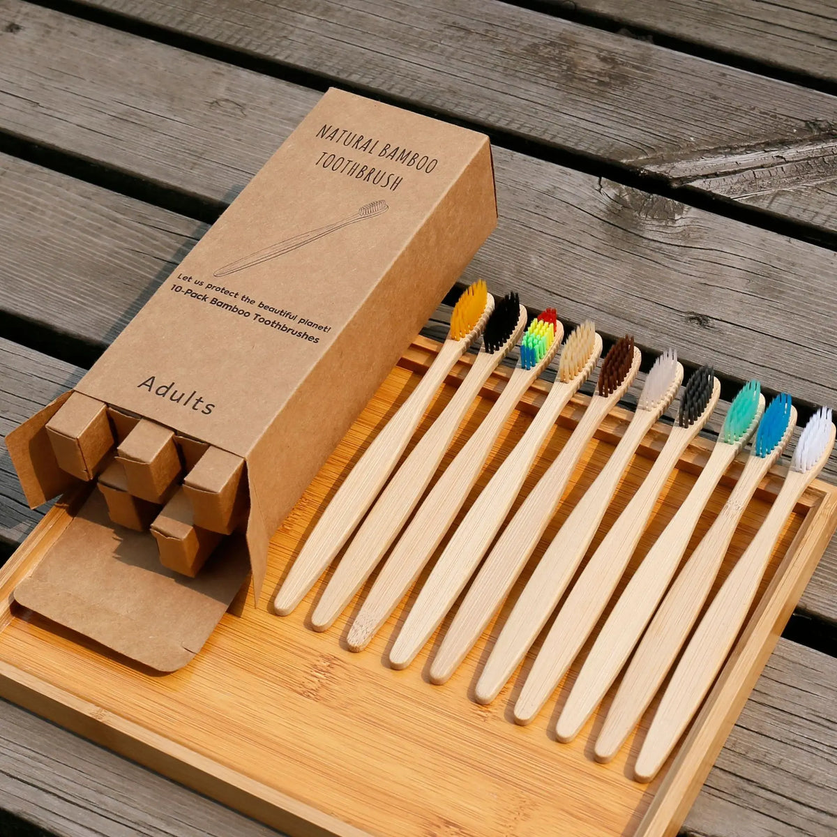 A wooden tray holds a set of natural bamboo toothbrushes packaged in a cardboard box.