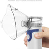 A hand is holding a clear handheld nebulizer mask device with a white and blue body, ready for operation.