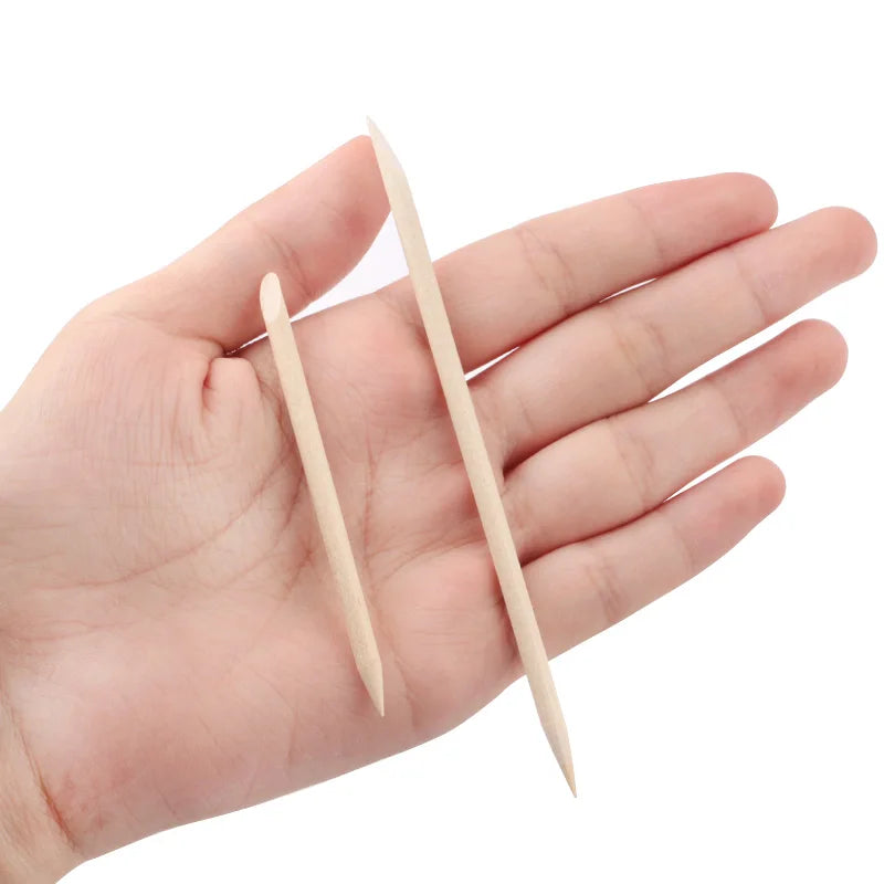 Two natural wood nail art pusher sticks held in a person's hand.