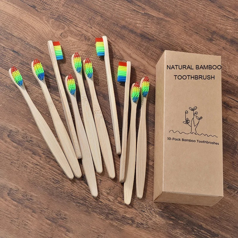 Une boîte contenant un pack de 10 brosses à dents en bambou naturelles à poils colorés, posées sur une surface en bois.