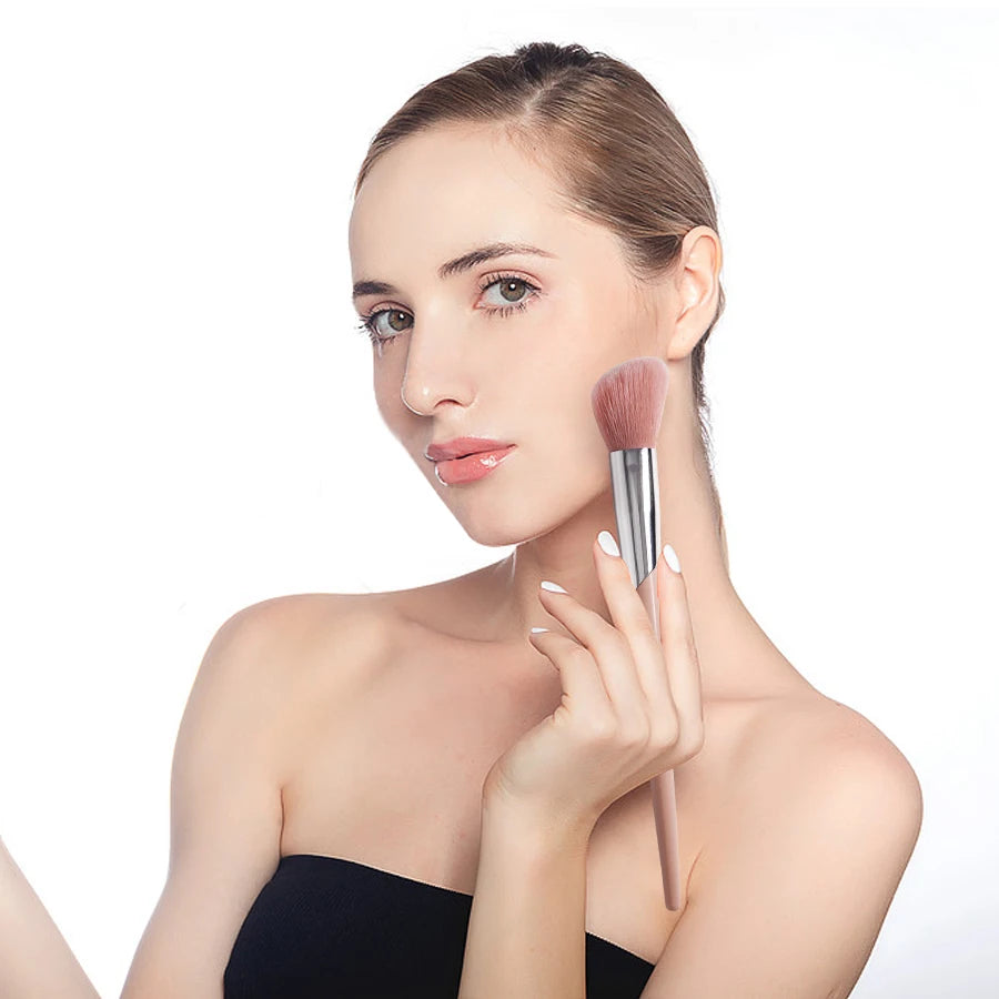 A close-up of a pink angled cheek blusher makeup brush held by a woman's hand.
