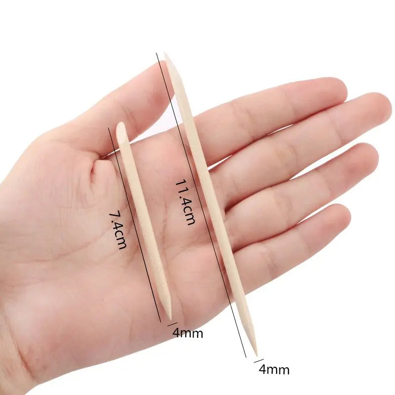 Two natural wood nail art pusher sticks are shown next to a hand for scale.