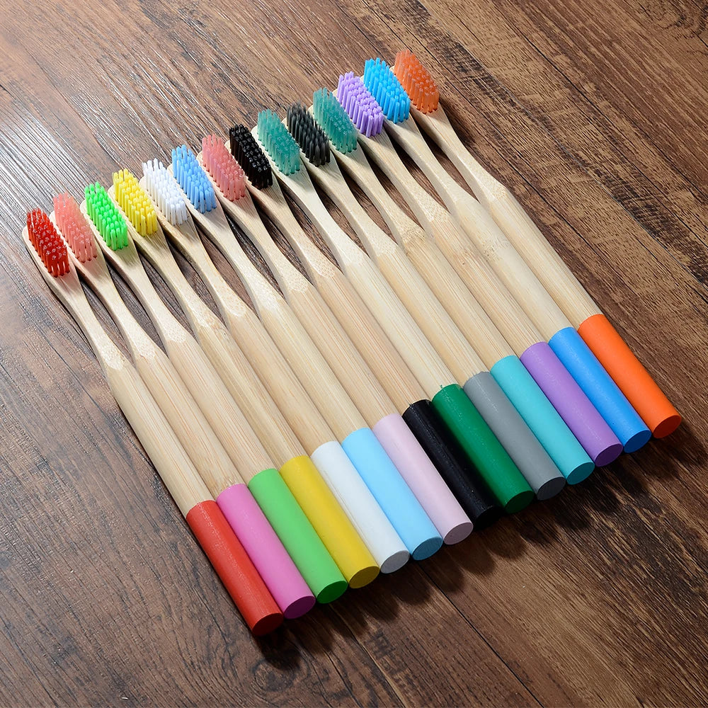 A collection of ten colorful bamboo toothbrushes with various bristles arranged diagonally on a wooden surface.
