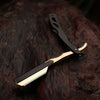 A professional straight edge barber razor with a black handle and a light wood blade rests on a dark surface.