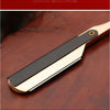 A professional straight edge barber razor with a black blade and gold accents resting on a dark wooden surface.