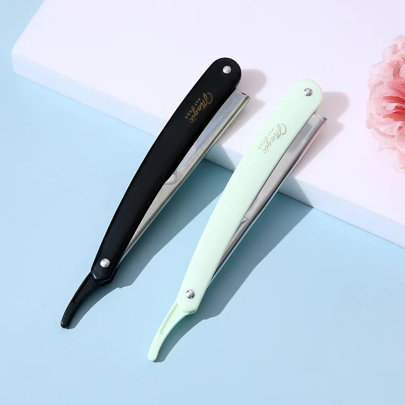 A folding straight razor shaver with black and light green handles is displayed on a light blue surface.