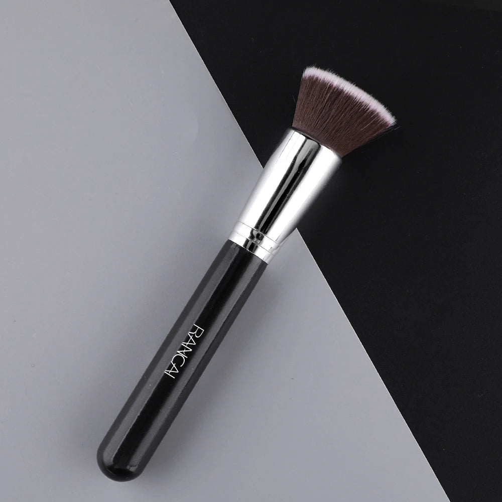 A black flat top kabuki foundation brush with a silver ferrule and bristles resting on a gray surface.