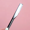 A silver folding straight razor shaver with a black handle is shown against a pink background.