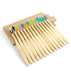 A wooden box holds a set of twenty colorful bamboo toothbrushes with various bristles.