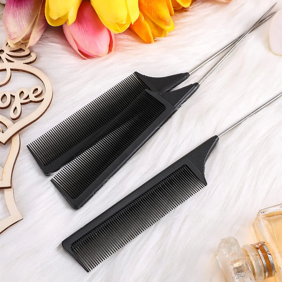 A set of black stainless steel rat tail hair combs displayed on a white surface with pink and yellow flowers.