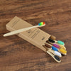 A wooden box contains a set of ten natural bamboo toothbrushes in various colors, packaged for oral hygiene.