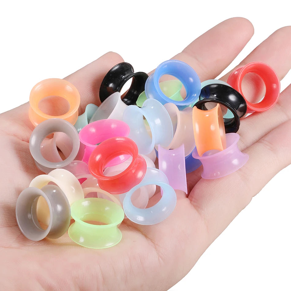 A hand holds a variety of colorful flexible silicone ear tunnels and plugs.