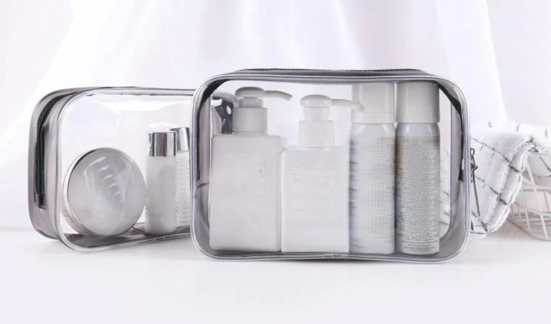 A clear waterproof travel cosmetic bag containing several white liquid bottles and a circular mirror.